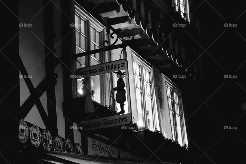 Black and white shot of illuminated windows of a souvenir shop in Quimper at night