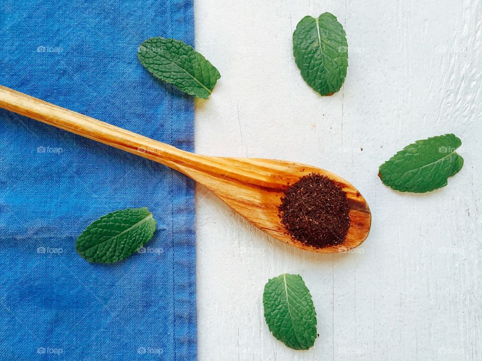 Dried tea leaves on wooden spoon with mint leaves