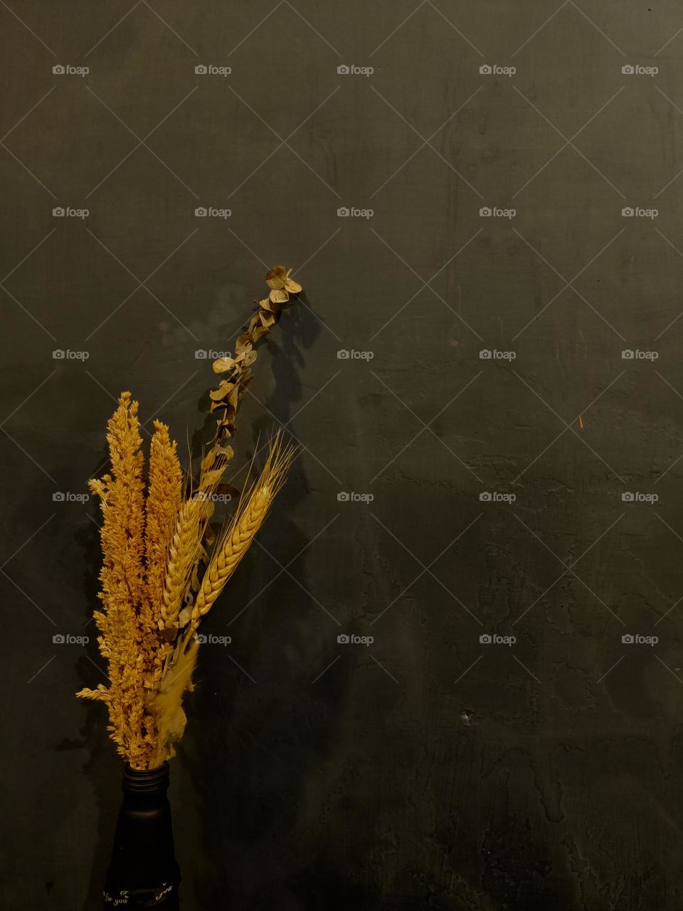 Dried flower bouquet in black glass bottle on wooden table against dull black wall background.Place for text or advertisement.View from abov