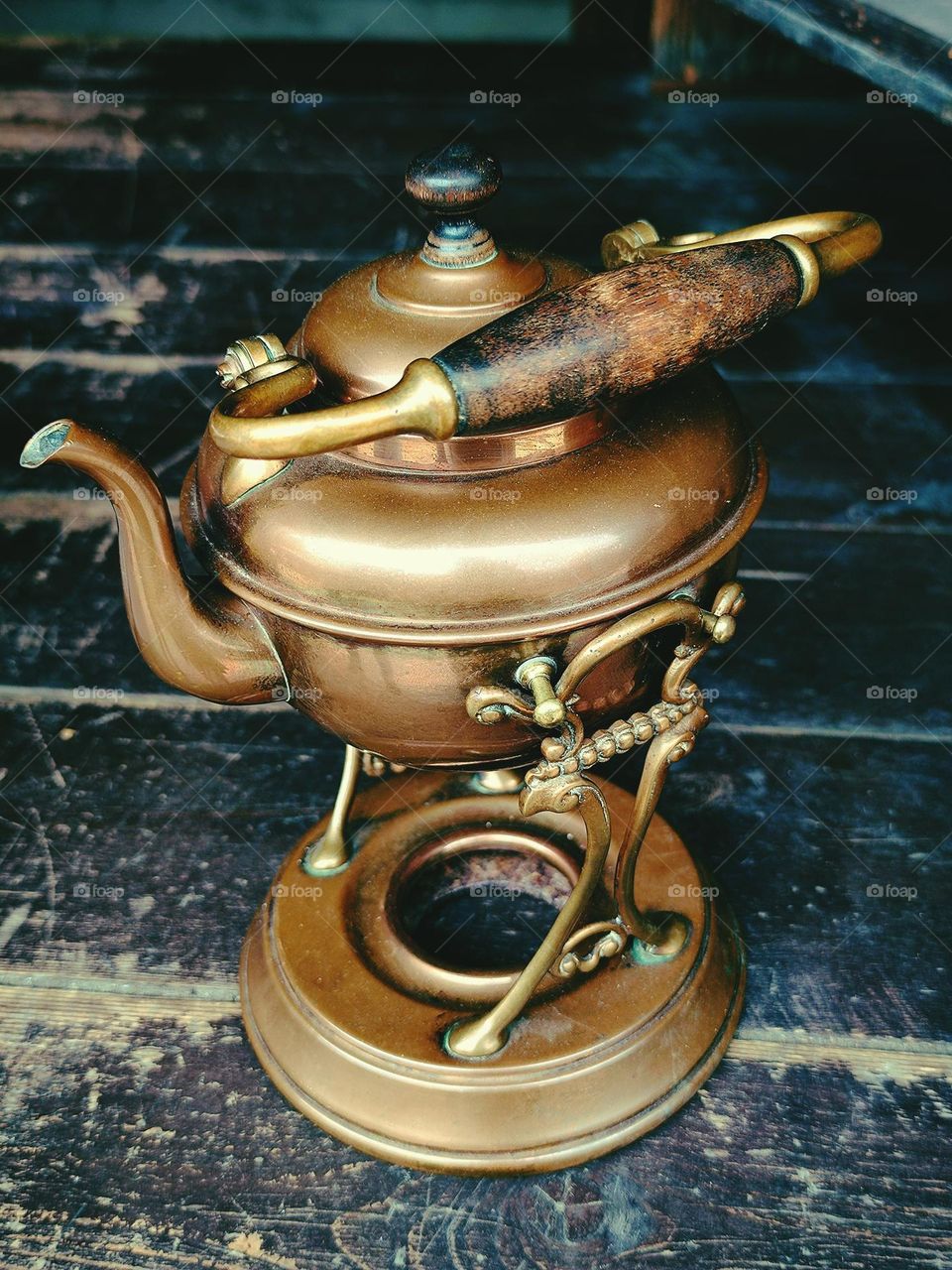 Metal. Antique copper teapot on copper spirit lamp.  Bouillotte.  Wooden background