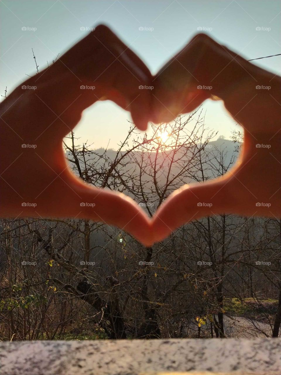 heart formed with hands with the setting sun inside