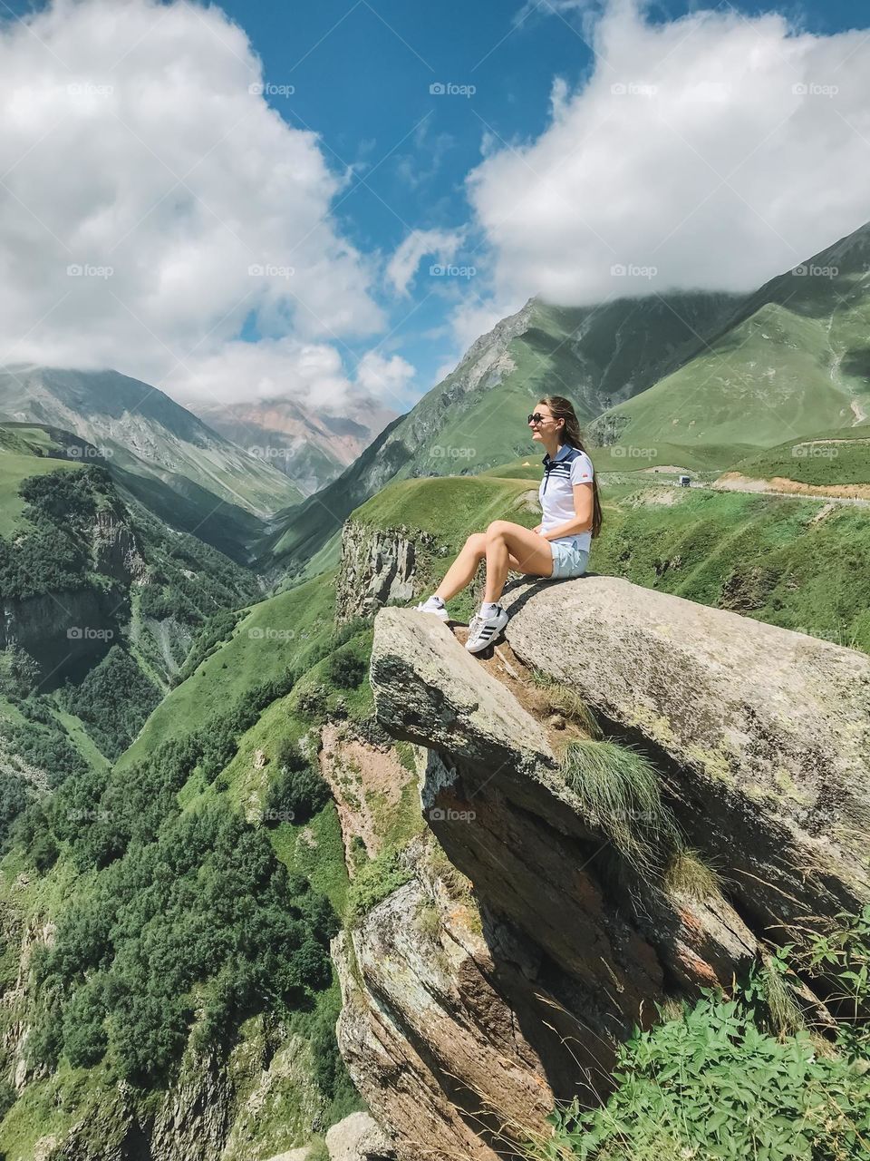 Young woman sitting on the rock edge enjoying mountain landscape