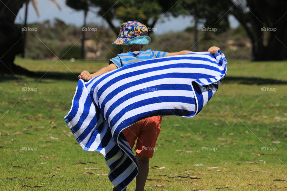 Little boy running across grass with beach towel pretending to be a super hero