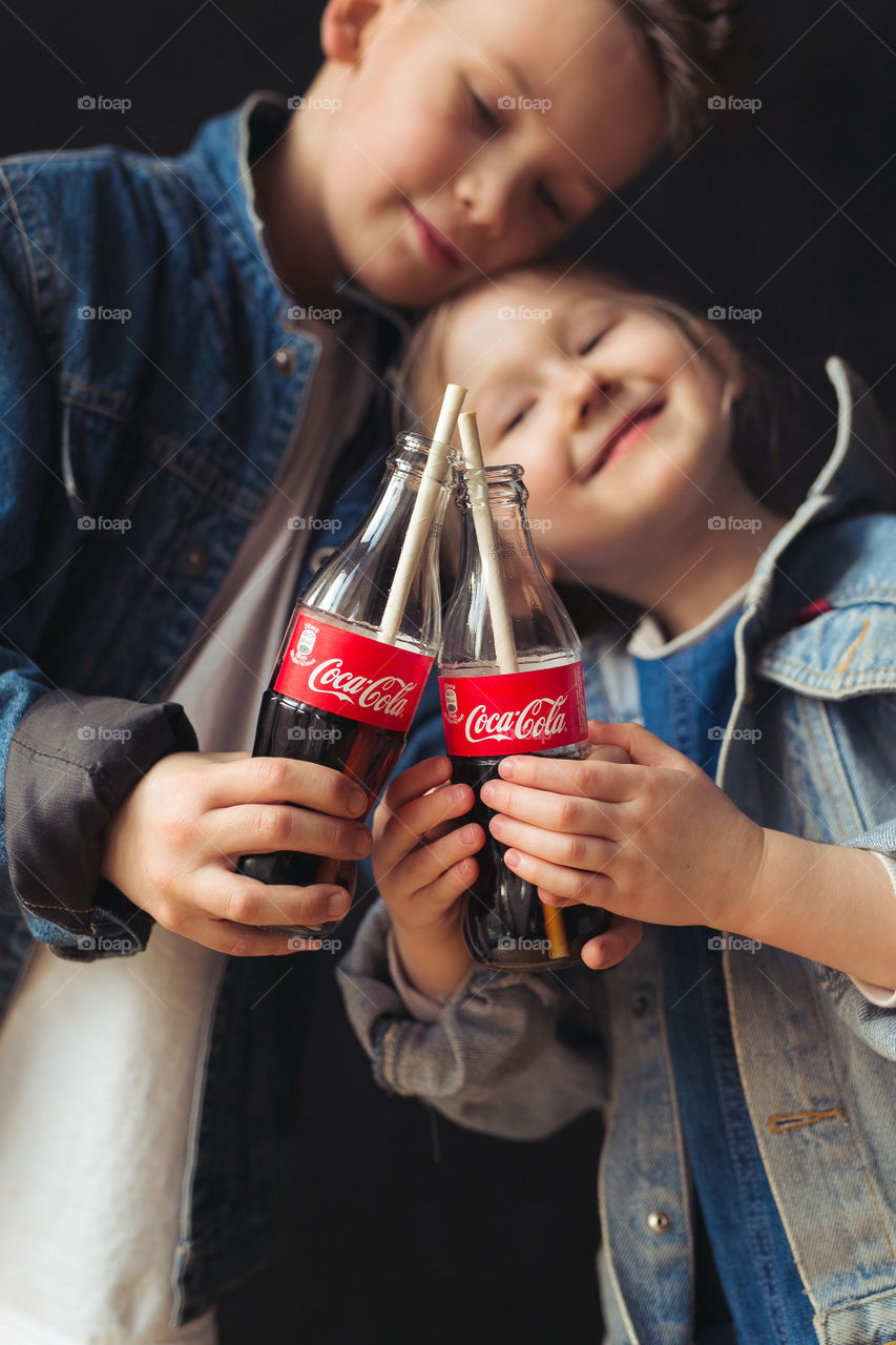 beautiful, stylish, fair-haired children, drinking Coca Cola, eating potatoes, dressed in denim clothes, free photo style. boy and girl have fun, rejoice, beautiful advertisement for coca cola drink