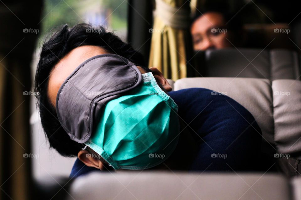 Portrait of a public bus passenger sleeping with a mask and eye mask on the passenger seat.