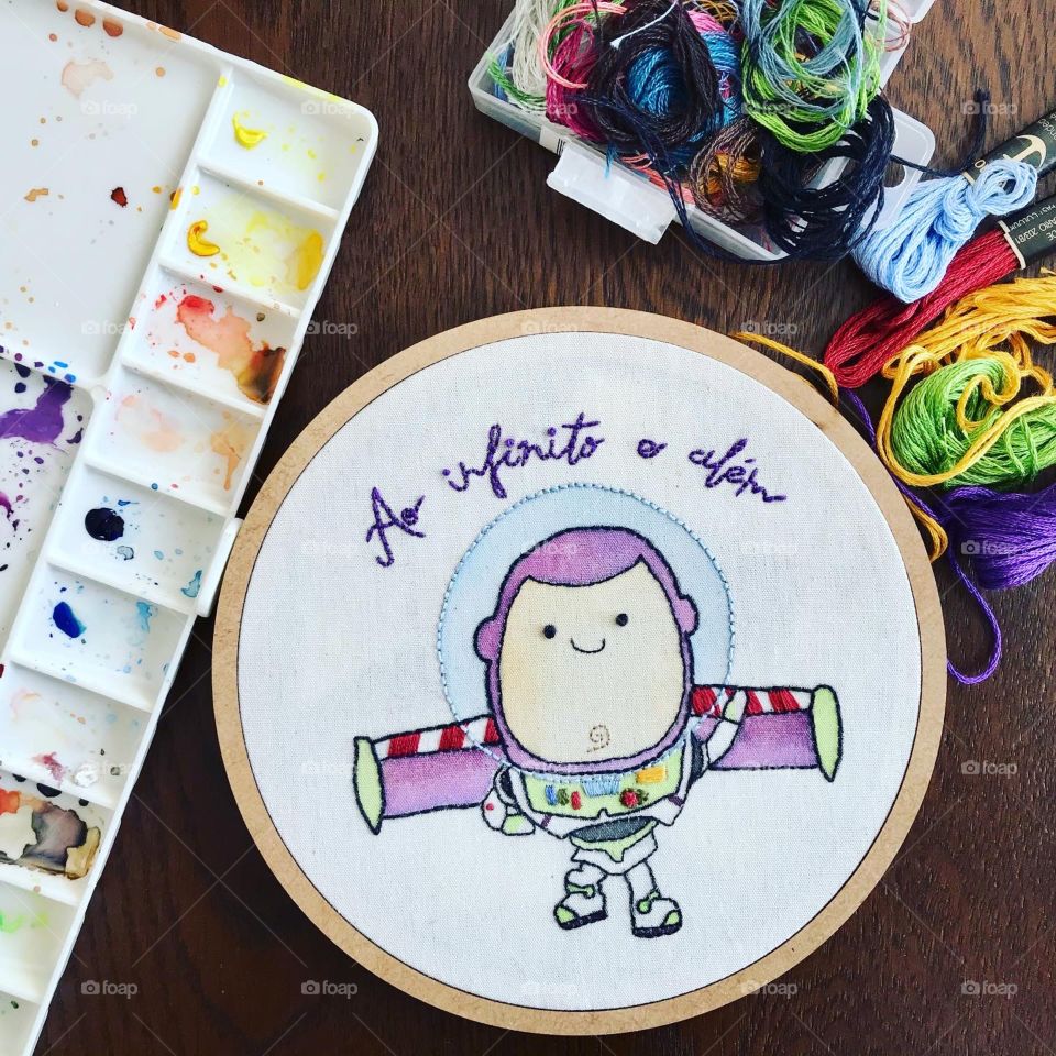 Embroidery made with lines and watercolors, it is possible to see the character from the movie Toy Story, Buzz ligthyear. The sentence to infinity and beyond is written in Portuguese.