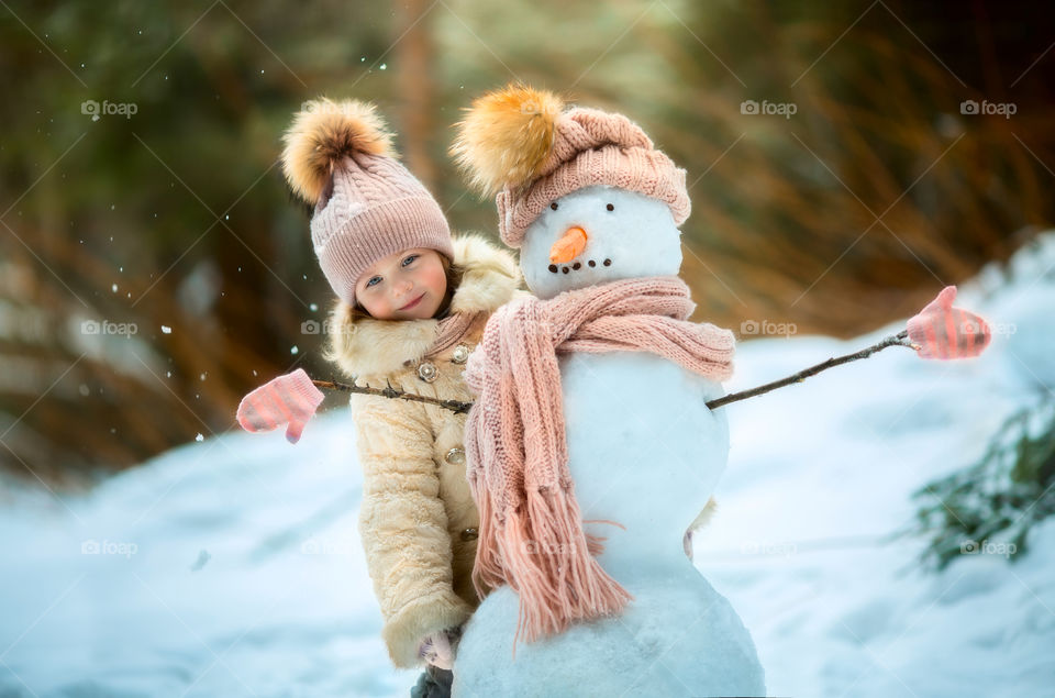 Little girl with snowman in winter forest at sunny day