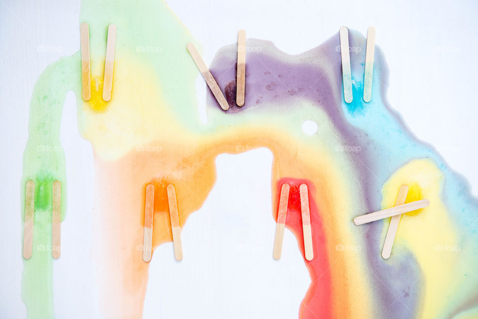 Flat lay of multi colored melted popsicles with the popsicle sticks left behind and colors mixed together