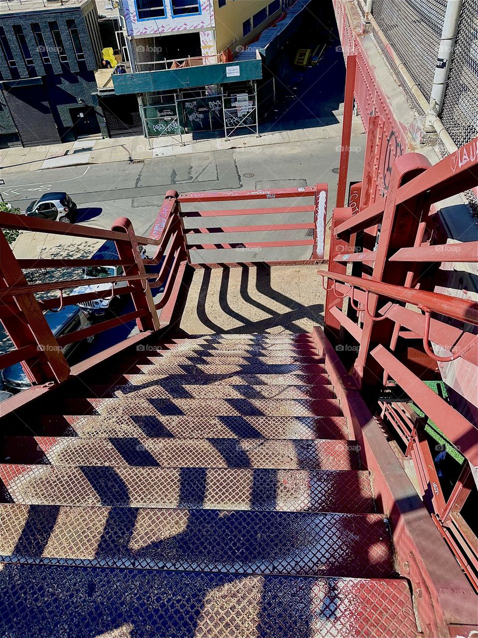 The red metal staircase of the “Pulaski Bridge” at “Newtown Creek” in “Greenpoint”, Bklyn has strong geometric features. When the sun casts shadows onto them they combine with the shapes to create intricate patterns. 2024. Hypnotic Productions