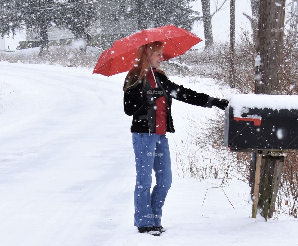 Woman with red Totes umbrella in the snow checking the mail