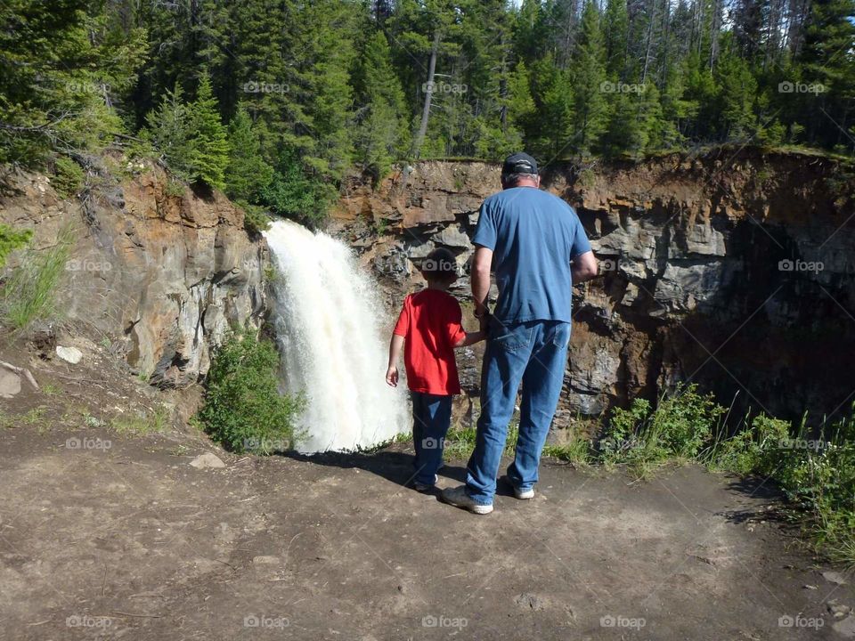 Father and son watching the breathtaking beauty of nature at the top of waterfall.