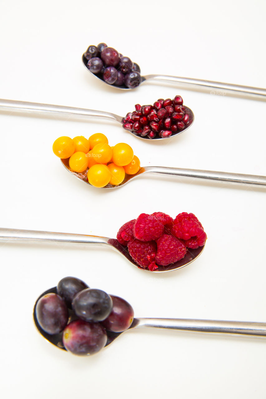 Variety of fresh colorful summer fruit arranged on silver spoons. Fresh fruit for a healthy diet and lifestyle. Close up on white background.