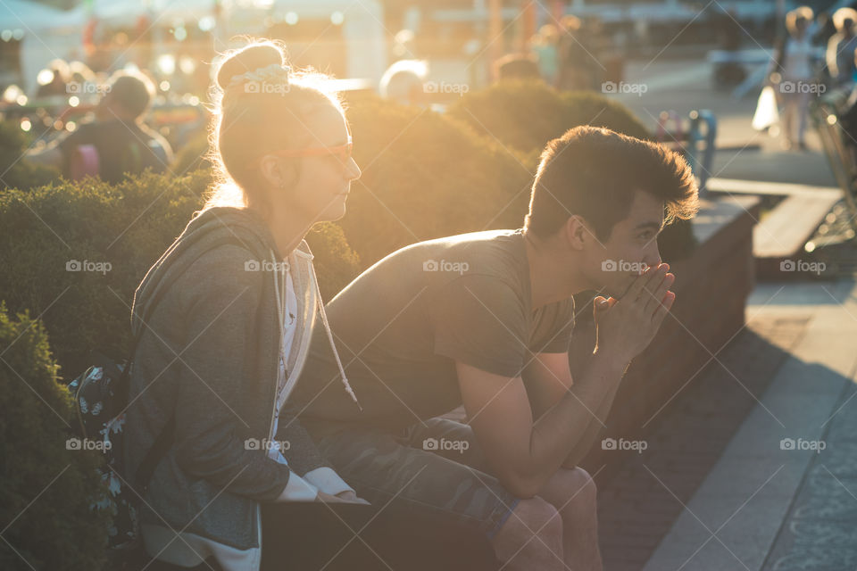 Couple of friends, teenage girl and boy,  having fun together, sitting in center of town, spending time together