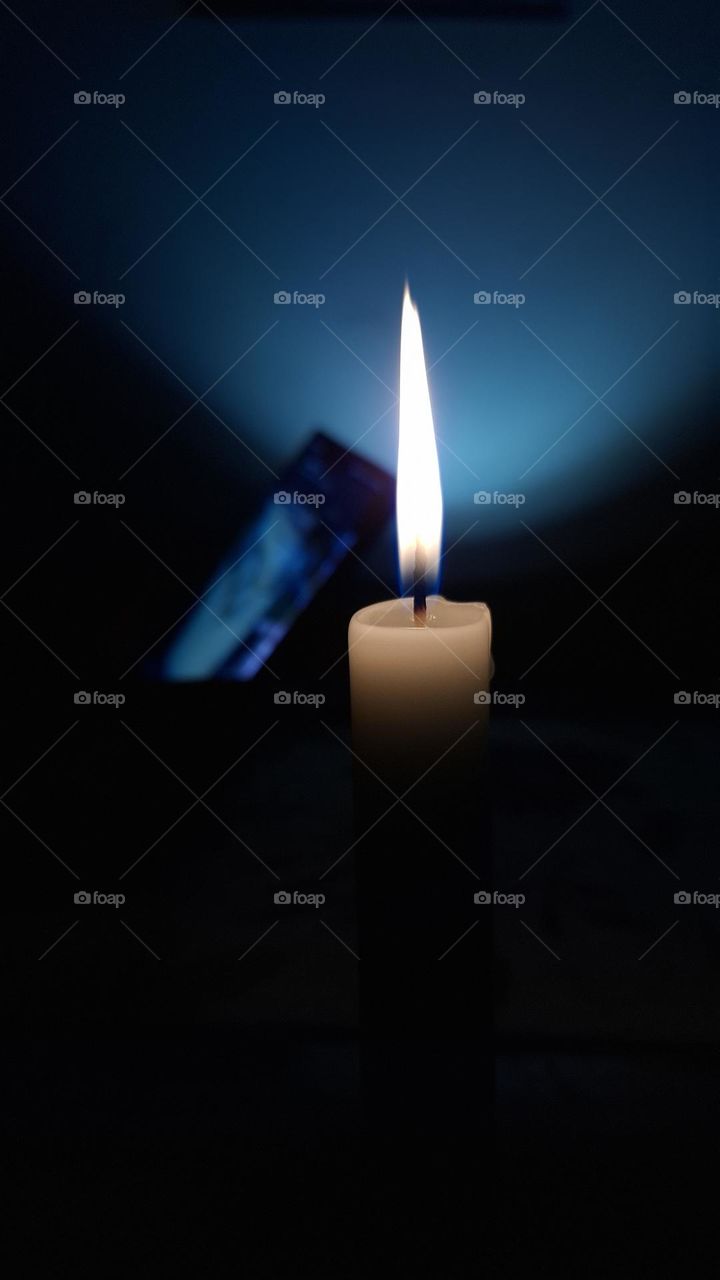 A solitary candle lights up the darkness, radiating a calm and mysterious glow. The flame symbolizes hope and introspection, while the soft blue background adds a peaceful, hypnotic contrast.