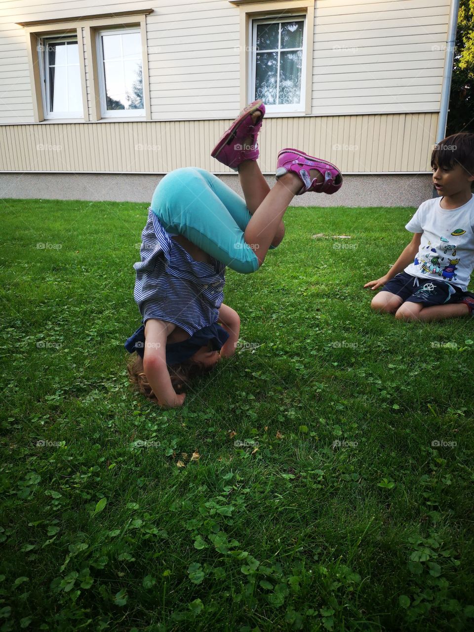 Girl standing on her head brother watching