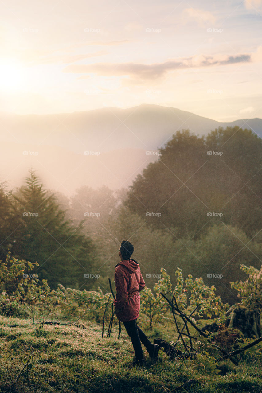 Boy enjoying a beautiful sunrise in the middle of the mountain in time of social estating