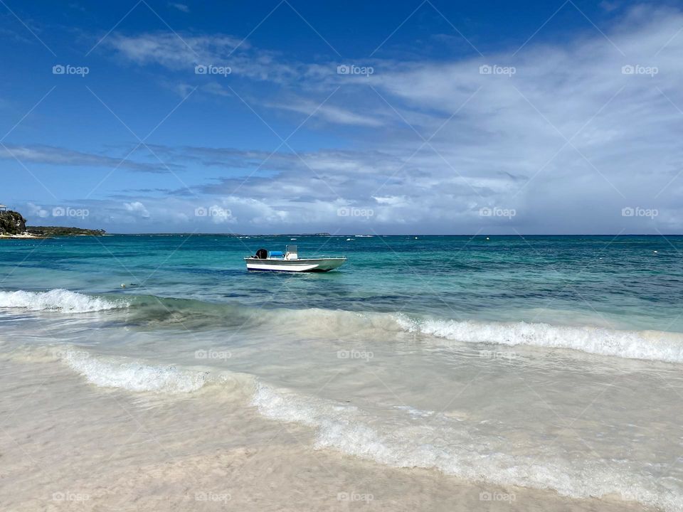 A small boat sitting just off a beach in clear blue water