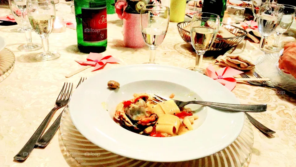 Paccheri pasta dish with tomato sauce,  mussels, a glass of white and a bottle of mineral water served in a restaurant of Ischia (Italy)