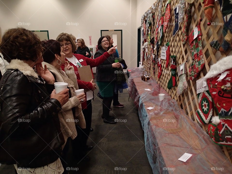 A crowd gathers at a holiday bazaar to view Christmas ornaments hanging on a wall. 
