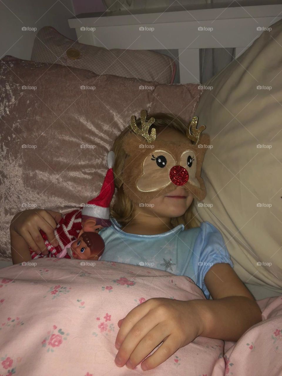 Little girl all tucked up in bed with her Santa’s reindeer sleeping mask on 