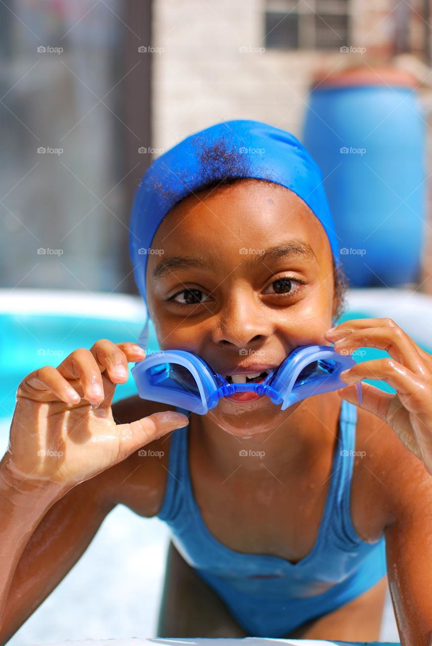 Girl of mixed race enjoying the refreshment of water in a swimming pool on a hot summer day, together with her little sister (family, fun, summer, water, blue, swimming suit, splash, hot, enjoy, play, outdoors)