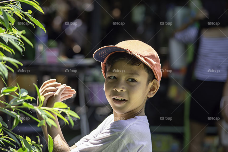 Portrait of Asian boy wearing a red cap and white  shirt is smile and Play water mist.