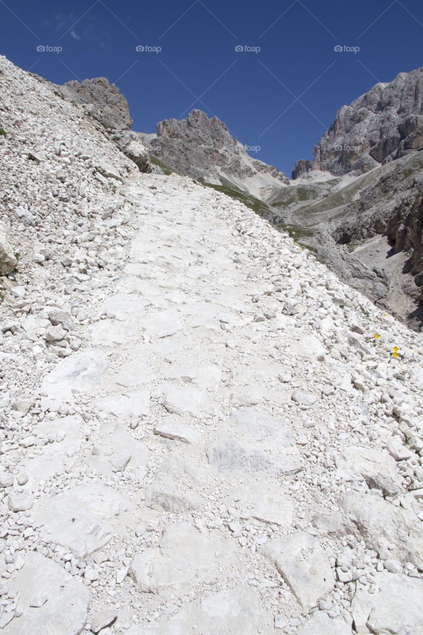 White rocky hiking trail to the mountain peak, blue sky 
