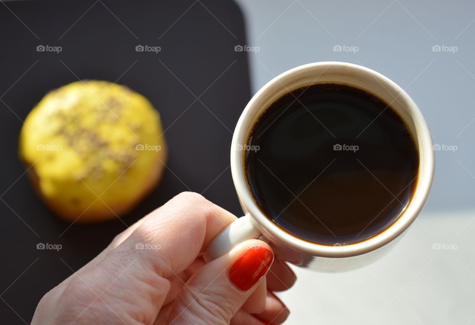 cup of coffee in female hand and bun sweet in sunlight on a white and brown background, morning routine