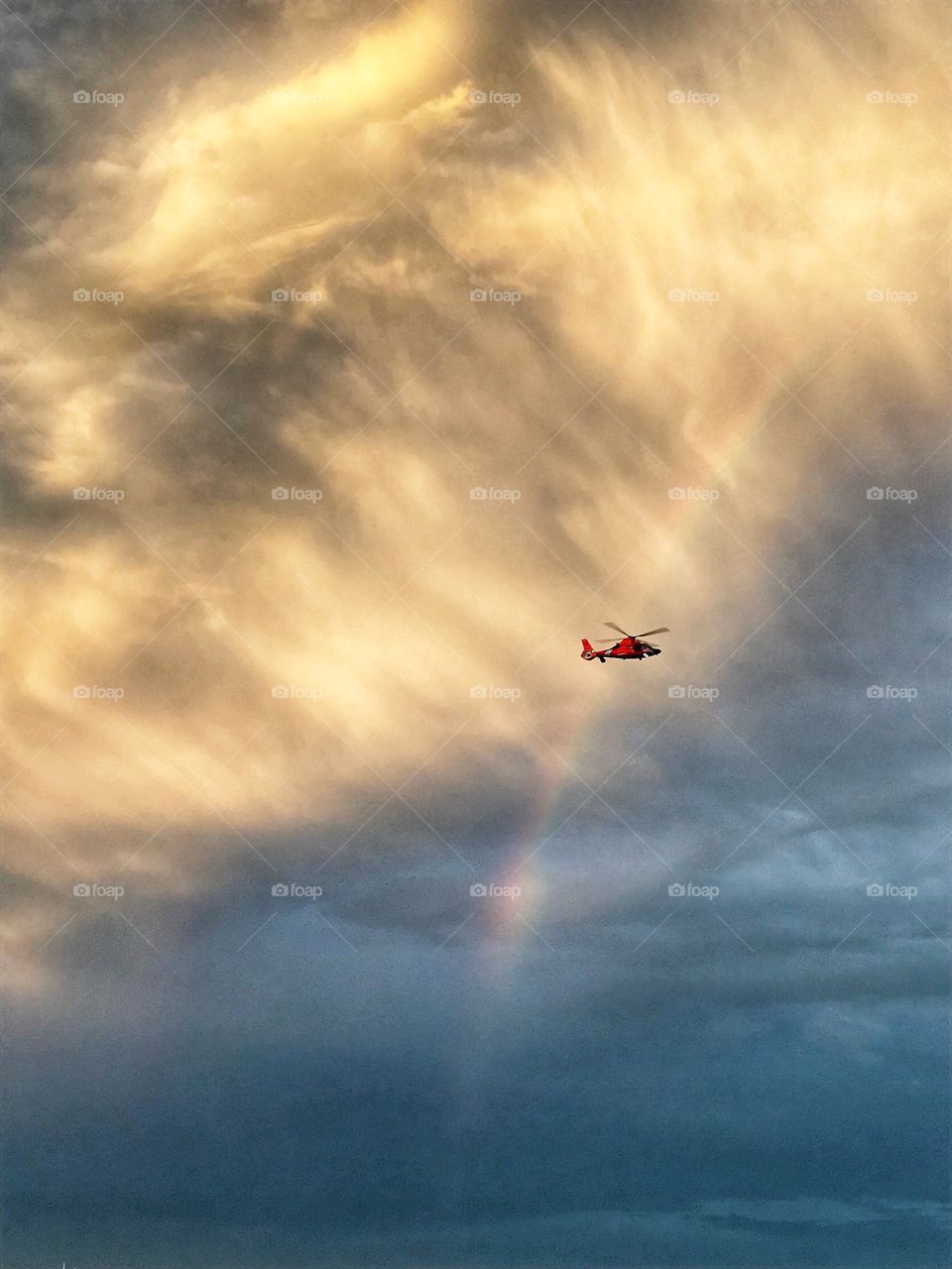 Watching a helicopter fly among clouds and a rainbow 