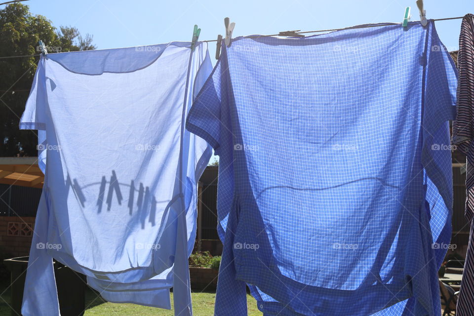 Hanging the laundry out to dry on sunny day, two men’s shirts, clothespins clothes pegs shadows on shirt