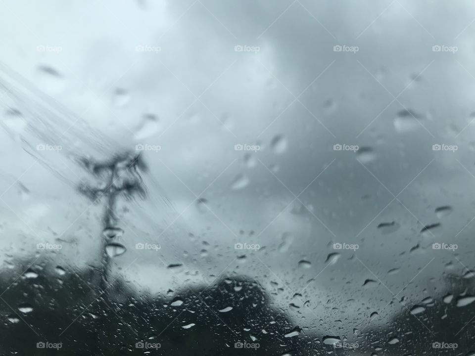 dark grey scene of countryside with electricity post and forest from car front windscreen when hardly raining and dark storm