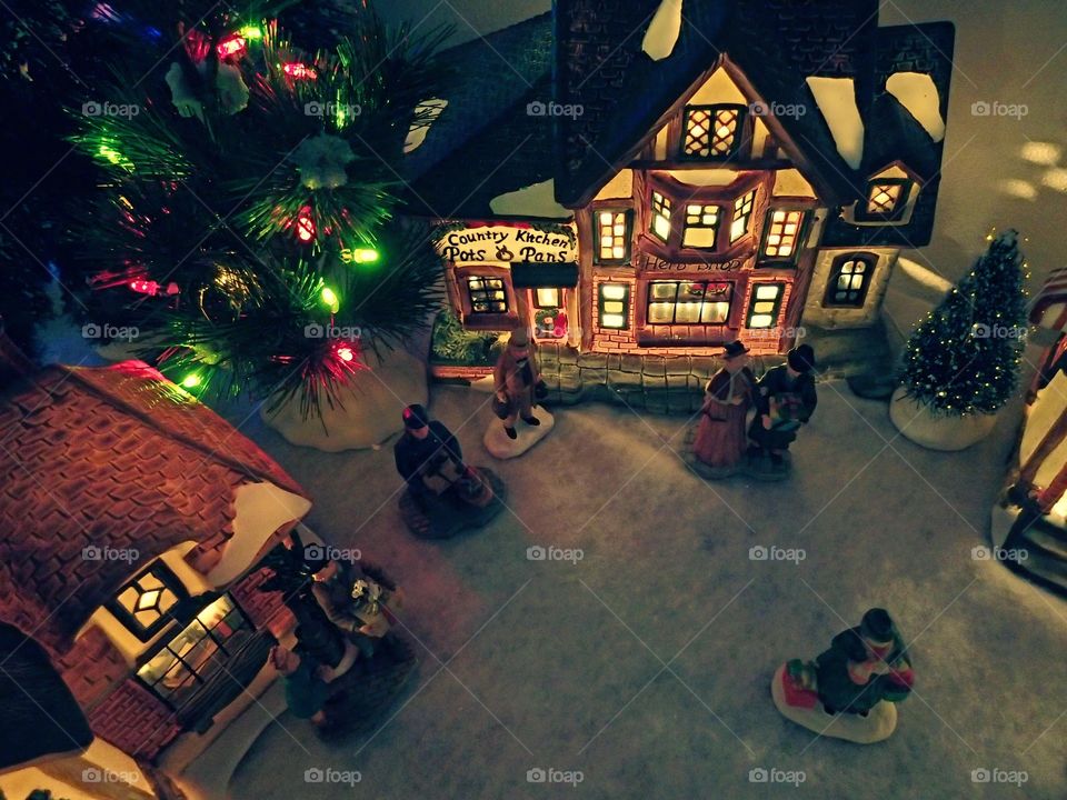 A Christmas village with a lit up store front, people, and Christmas tree. 