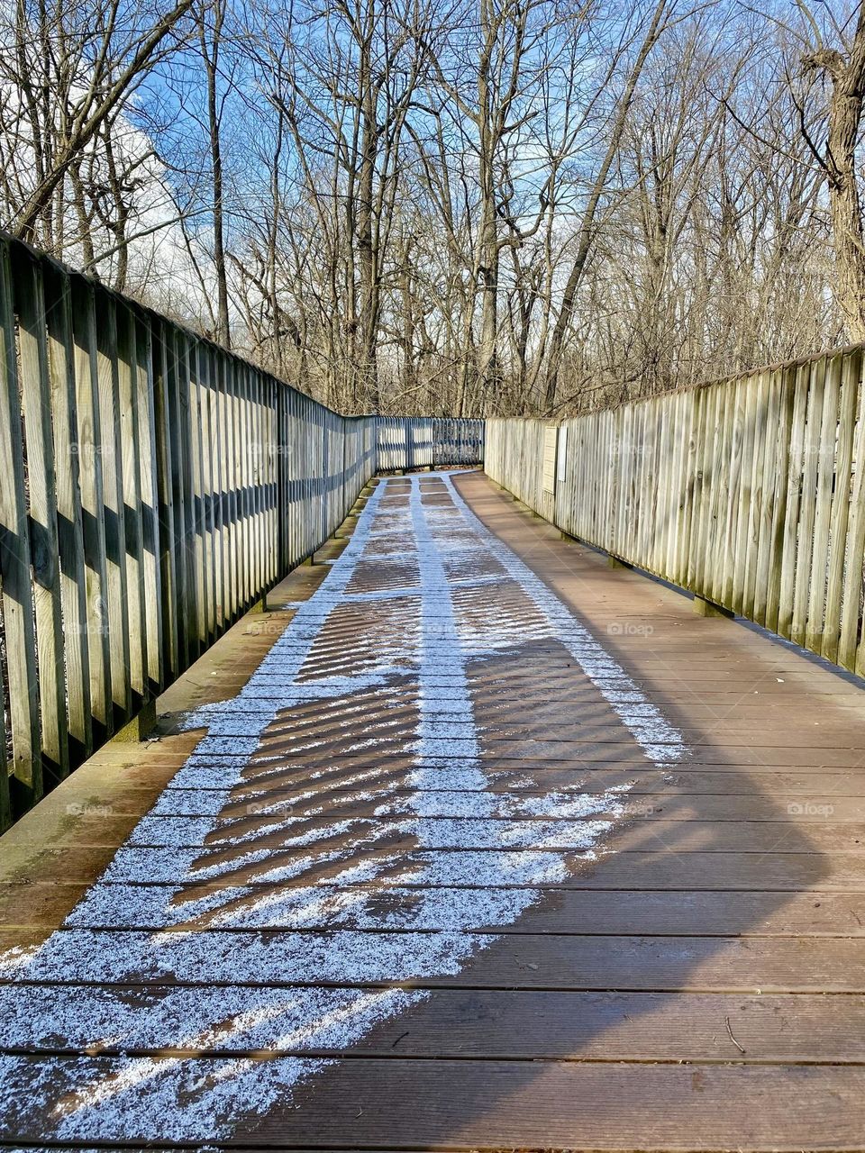 Snow and shadows on a boardwalk around a quarry lake at a local park 