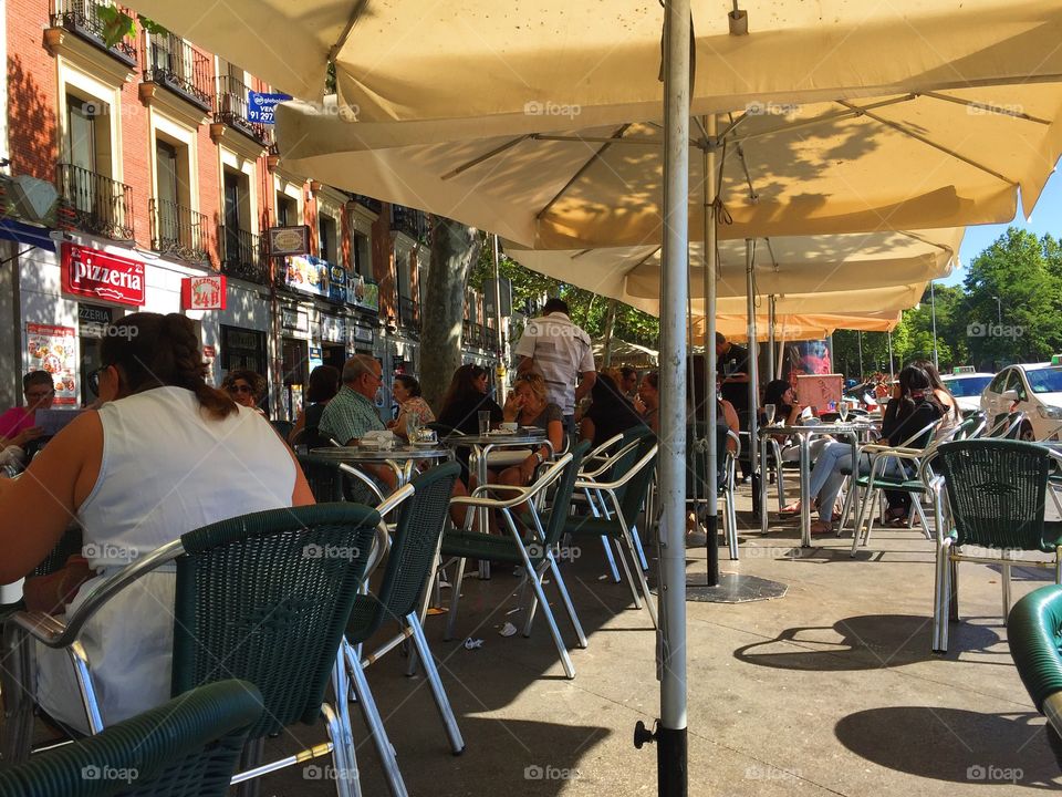 People sitting at an outdoors restaurant in the shadow ,the in the summer in Madrid 