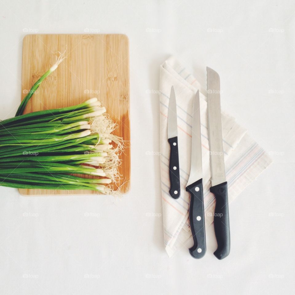onions, knives cutting board. Green onions on a cutting board and different knives on a towel next