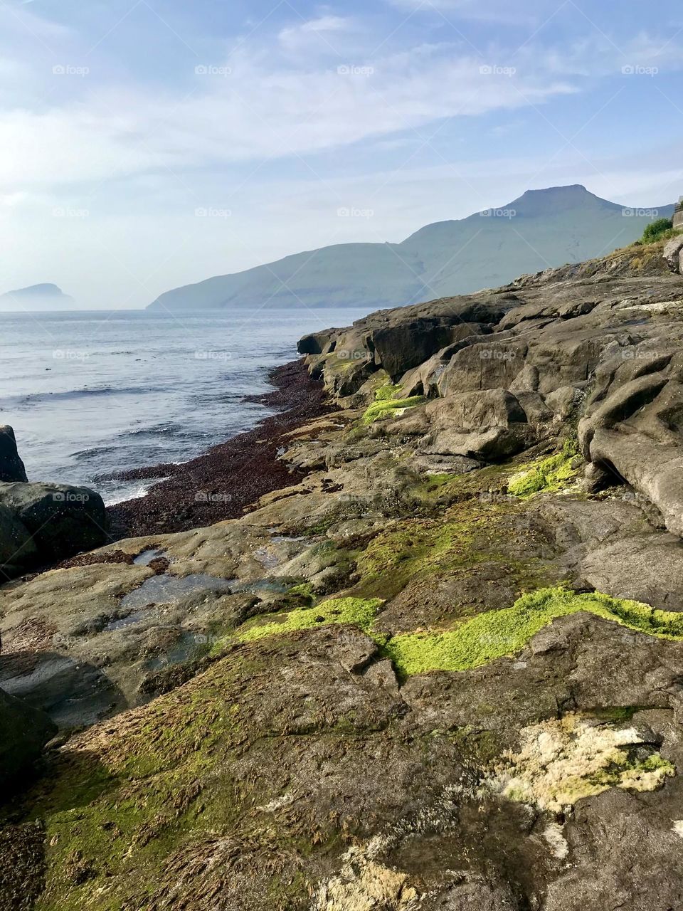 Luminous green rocks and cold sea with mountain and island view in the Faroe Islands