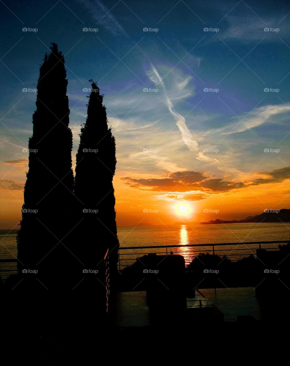 Vivid sunset across the bay of Dubrovnik with silhouette of cypress trees