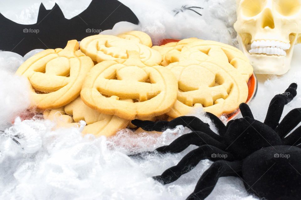 Halloween pumpkin-shaped cookies with some decoration: a bat, a spider and a skull.