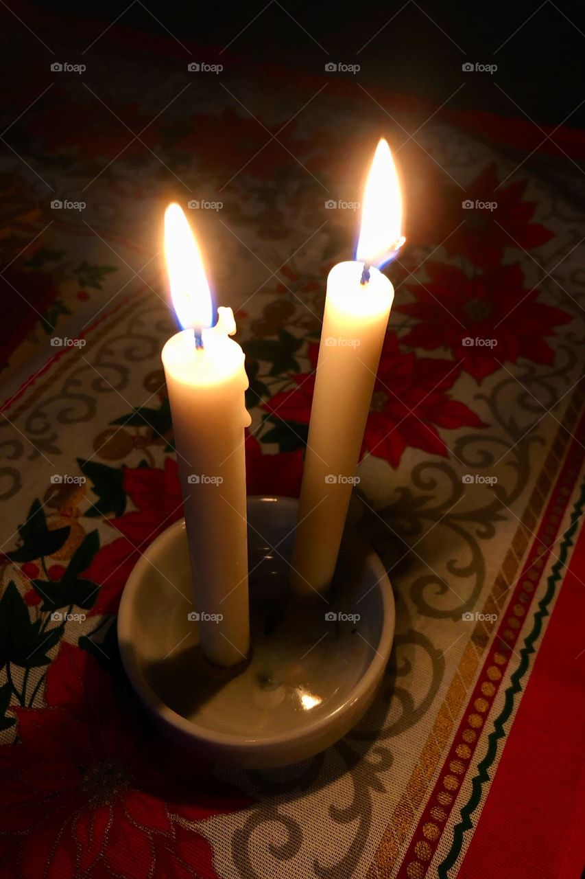 Two lit candles on the table over a Christmas theme cloth