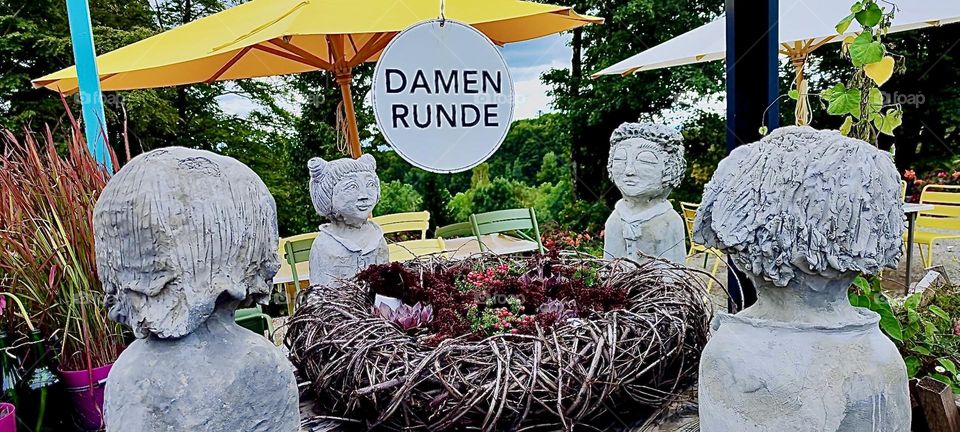 “Damen Runde” or “Ladies Circle” refers to sculptures around a basket filled with flowers. It is a humorous presentation at the “Bayerische Landesgartenschau”, the “Bavarian State Garden Show” in “Freyung”, Germany. 2023. Hypnotic Productions
