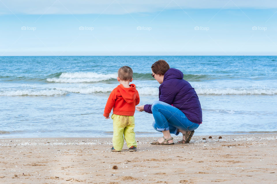 Parent with child at sandy beach collecting seashells.