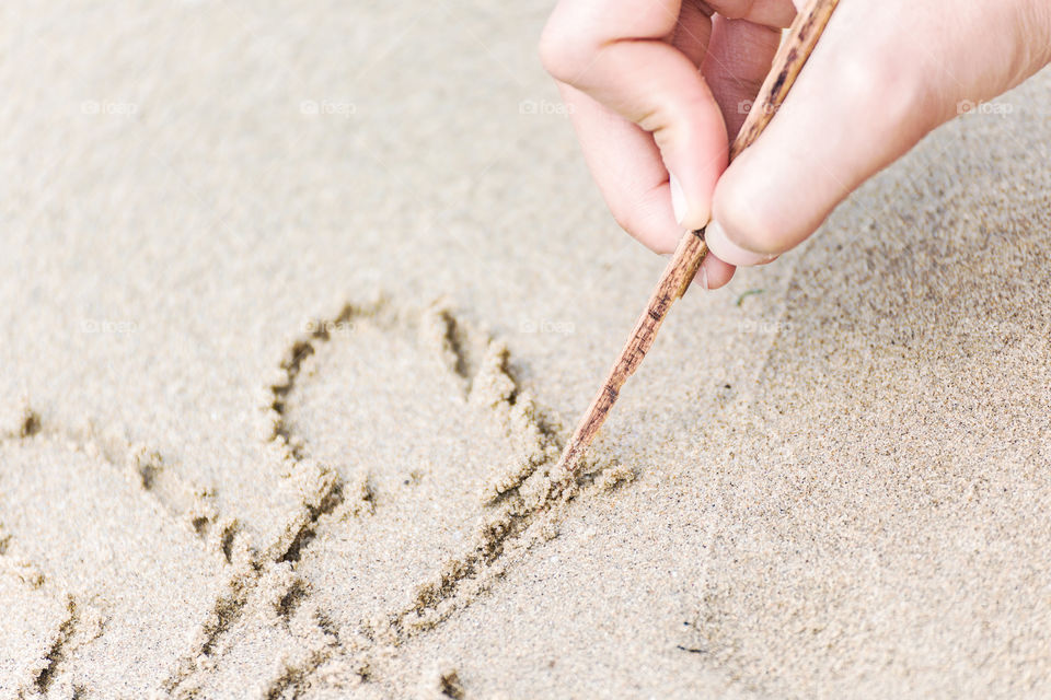 hand use stick writting heart on sand.