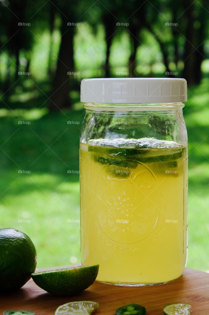 Refeshing lime-and-jalepeño-flavored kombucha, rebottled in a quart-size mason jar for a second ferment, with slices of lime and jalepeño on a bamboo cutting board, against a blurred outdoor background in summer