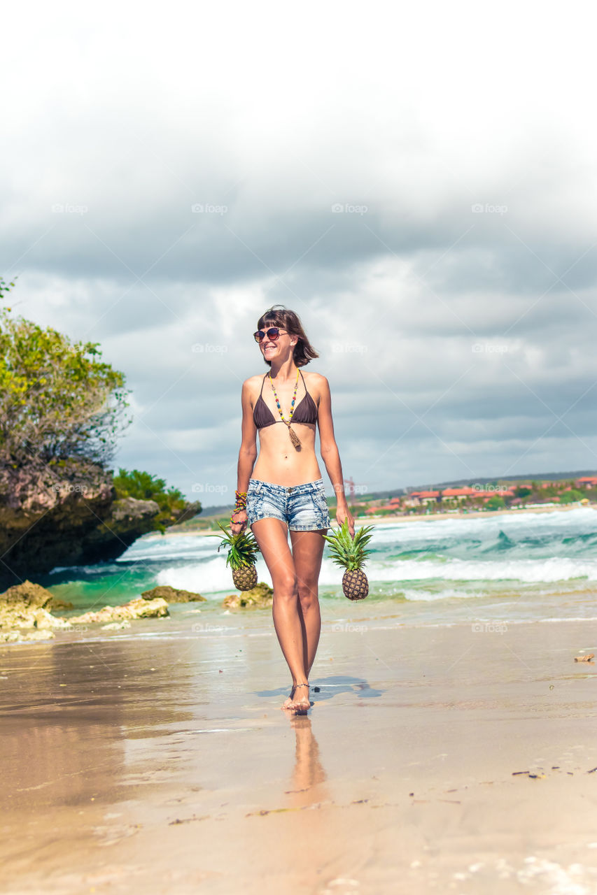 A girl walks along the beach and holds pineapples in her hands. Bali island.