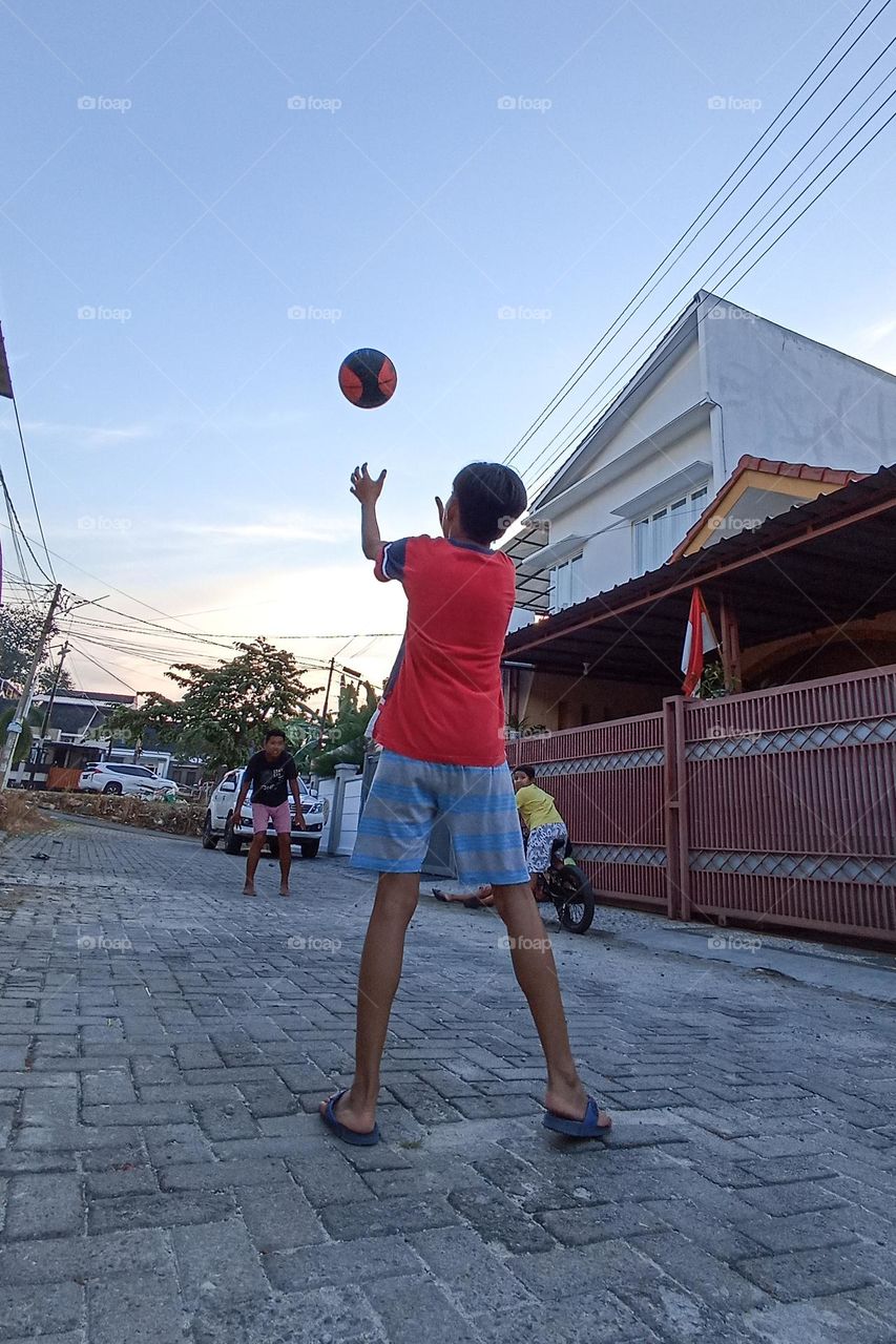 Bandar Lampung, Lampung, Indonesia - December 15, 2023: someone playing ball on the street, with a backdrop of buildings and a clear sky