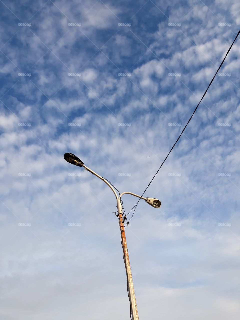 Two tall street lamps under the blue sky