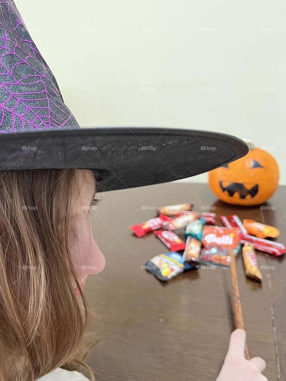 Girl dressed as a witch looking at Halloween candy and a pumpkin.