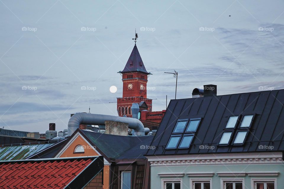 Early morning view over the city while the moon is keeping the town hall clock company 