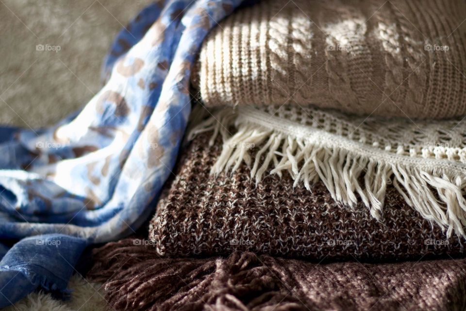 Cable knit, crocheted and fringed sweaters in taupe and brown and a blue tye-dyed leopard-print scarf on a sheepskin throw 