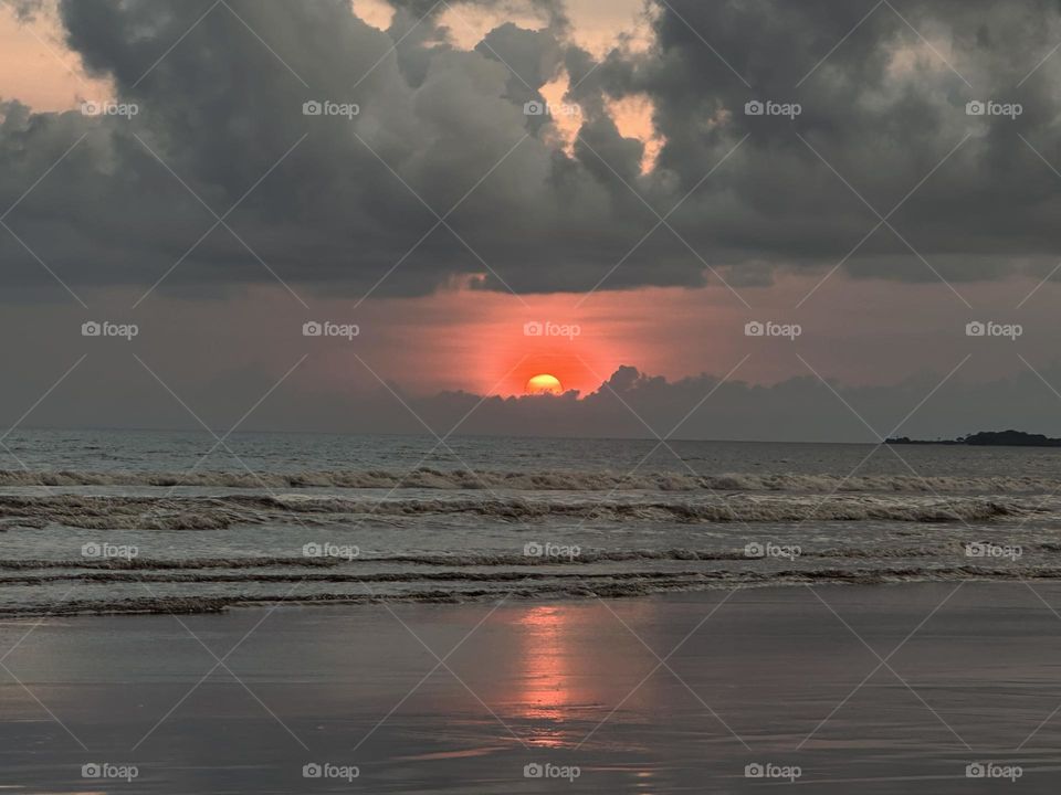 Beautiful and amazing orange sunset on the beach reflecting on the beachfront in a cloudy day.